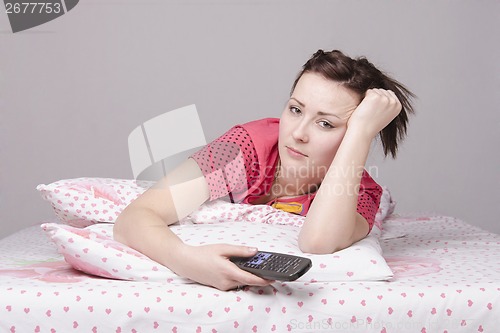Image of The tired girl lying in bed and watching TV