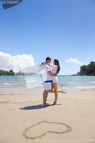 Image of happy couple have fun on the beach with heart on sand