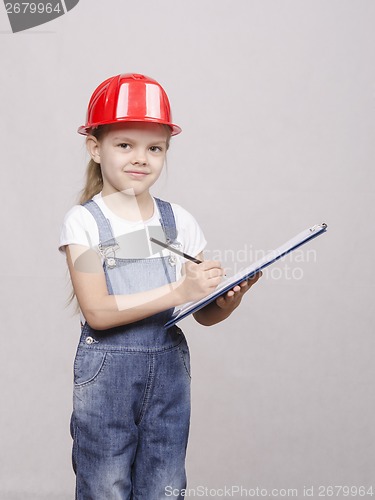 Image of engineer child stands helmet and writes in folder