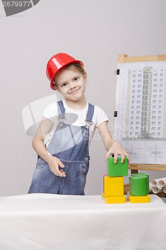 Image of Girl Builder in helmet builds a house on drawing