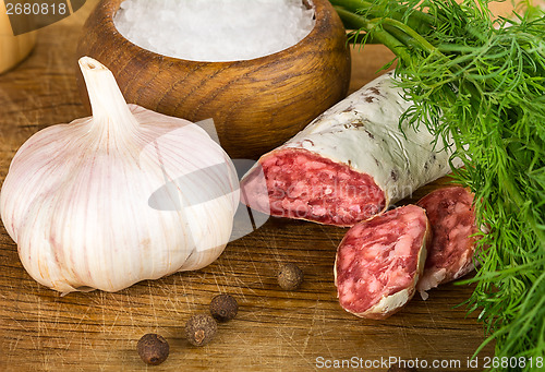 Image of sliced salame on cutting board, with dill, pepper, salt