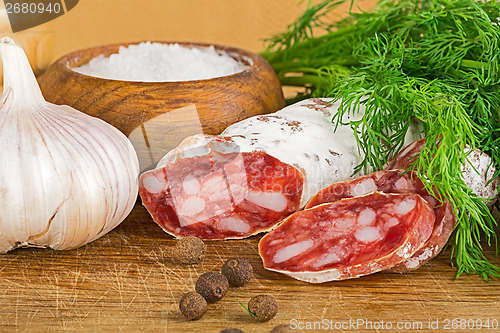 Image of sliced salame on cutting board, with dill, pepper, salt