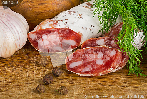 Image of sliced salame on cutting board, with dill and pepper