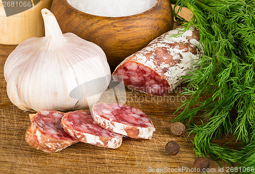 Image of sliced salame on cutting board, with dill, pepper, salt