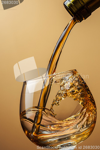 Image of Cognac pouring from bottle into glass with splash on brown backg