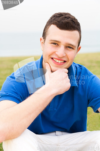 Image of Happy young man sitting on lawn