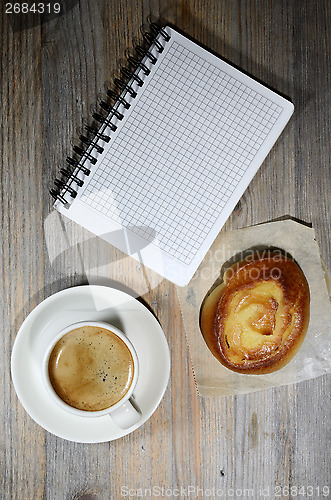 Image of cup of espresso, checkered notebook and bun