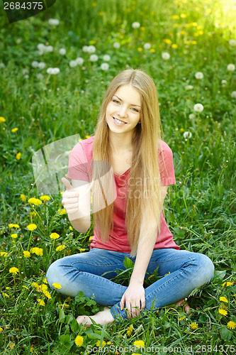 Image of Smiling female sitting on the field of dandelions