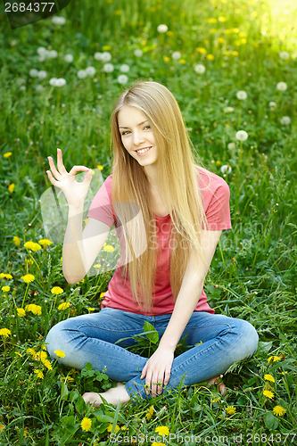 Image of Smiling female sitting on the field of dandelions