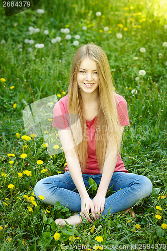 Image of Smiling female sitting on the field of dandelions