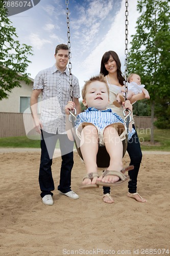 Image of Father And Mother Pushing Boy On Swing