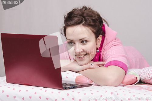 Image of Cheerful girl in bed works for laptop