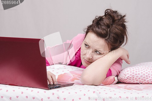 Image of Girl in bed with alarm looks laptop