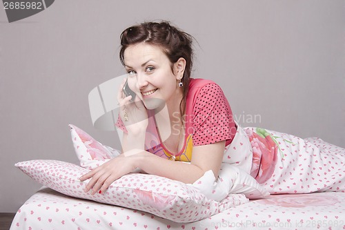 Image of girl smiles talking on phone in bed