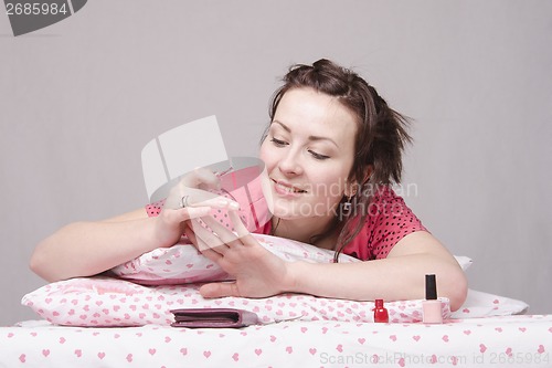 Image of girl paints nails, lying in bed