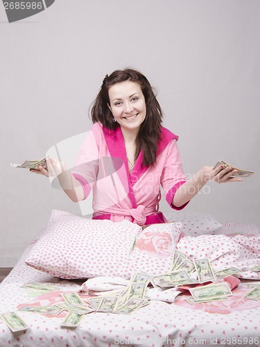 Image of Joyful girl sitting on bed with a bundle of money