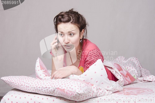 Image of Young girl talking on the phone in bed