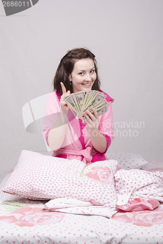 Image of Happy girl sitting in bed with a bundle of money