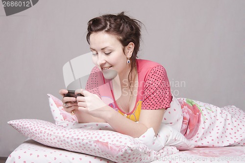 Image of Happy girl writes SMS in bed