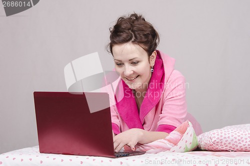 Image of Happy girl in bed works for laptop