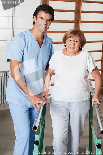 Image of Therapist Assisting Senior Woman To Walk With The Support Of Bar
