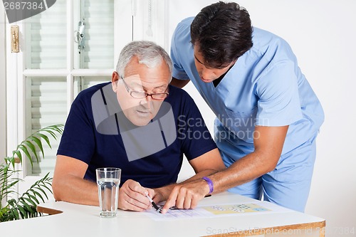 Image of Male Nurse Helping Senior Man In Solving Puzzle