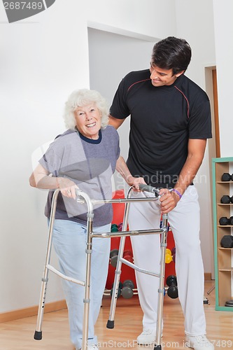 Image of Senior Woman Holding Walker While Trainer Assisting Her