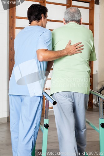 Image of Therapist Assisting Senior Man To Walk With The Support Of Bars