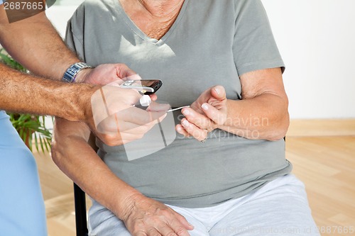 Image of Man Checking Blood Sugar Level Of Patient