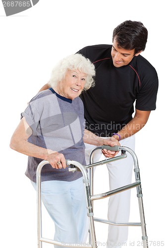 Image of Senior Woman Holding Walker While Trainer Assisting Her