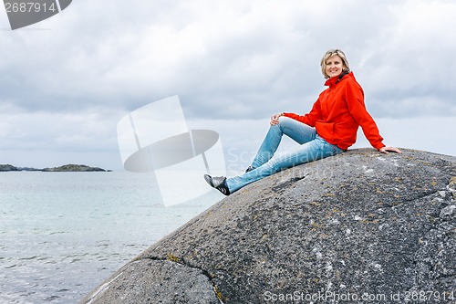 Image of Woman sitting on stone against sea background