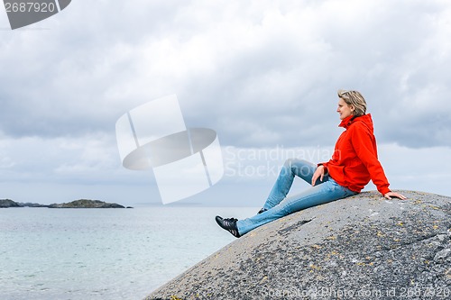 Image of Woman sitting on stone and enjoying sea view