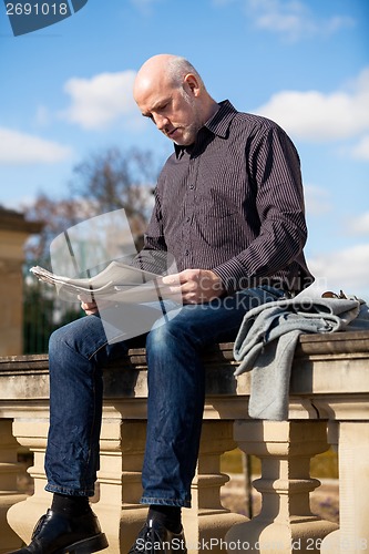 Image of Man sitting reading a newspaper on a stone wall