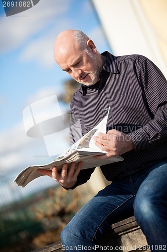 Image of Man sitting reading a newspaper on a stone wall