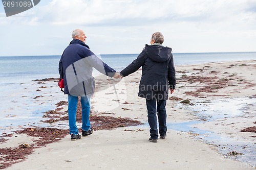 Image of happy elderly senior couple walking on beach