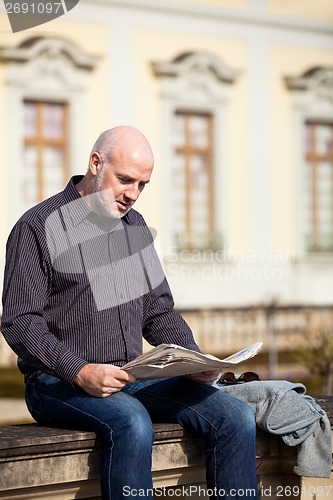 Image of Man sitting reading a newspaper on a stone wall