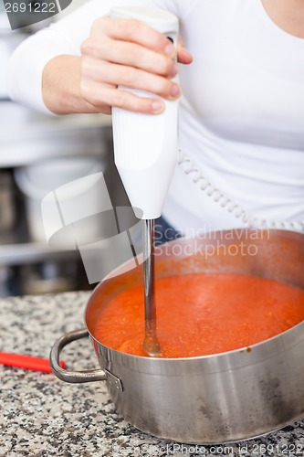 Image of Woman chef whisking boiled tomato sauce in a pot