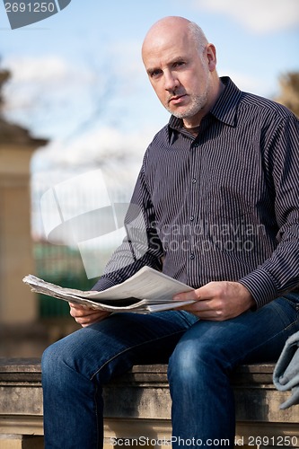 Image of Man sitting reading a newspaper on a stone wall