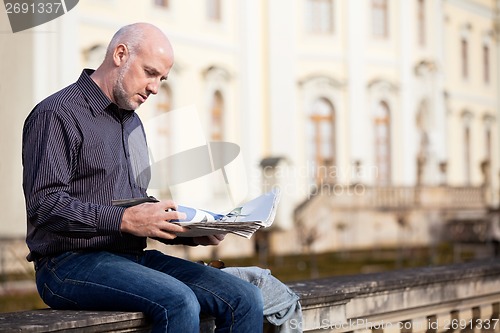 Image of Man sitting reading a newspaper on a stone wall