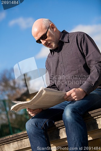 Image of Man sitting reading a newspaper on a stone wall