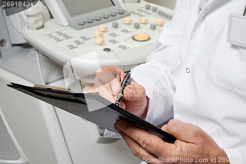 Image of Male Doctor Writing On Clipboard