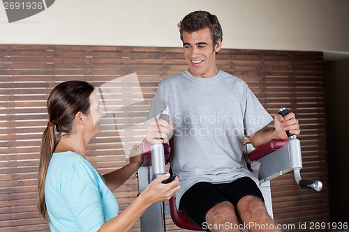 Image of Man Using An Exercise Machine While Looking At Instructor