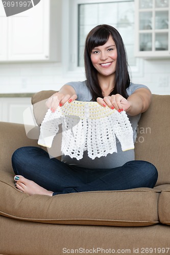 Image of Pregnant Woman Holding Baby Clothing On Sofa