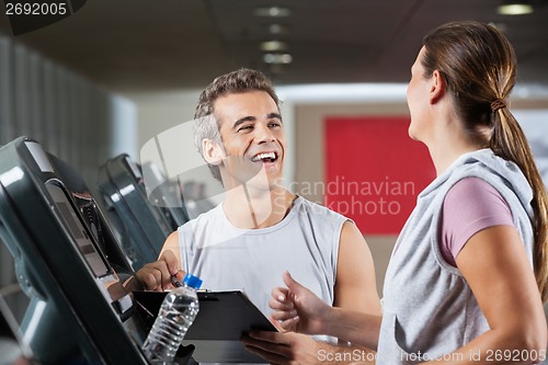 Image of Happy Instructor Looking At Female Client Exercising On Treadmil