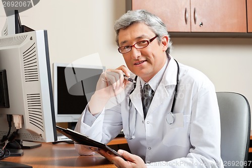 Image of Doctor Sitting At Desk In Front Of Computer