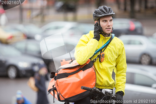 Image of Male Cyclist With Courier Bag Using Mobile Phone On Street