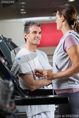 Image of Instructor Looking At Female Client Exercising On Treadmill