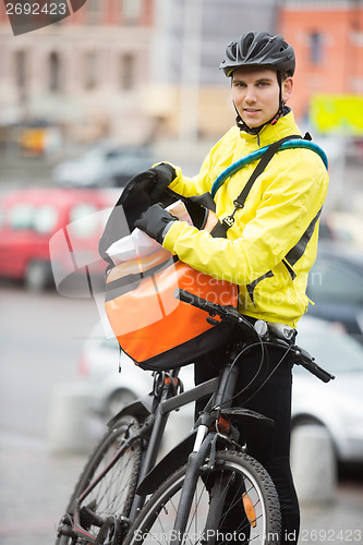 Image of Male Cyclist Putting Package In Courier Bag On Street