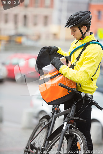 Image of Young Male Cyclist Putting Package In Courier Bag