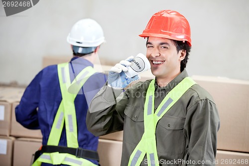 Image of Foreman Drinking Coffee While Colleague Working At Warehouse